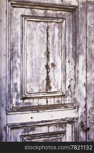 A detail view of an old, weather-beaten wood door with layers of peeling gray paint results in a distressed, weathered texture.