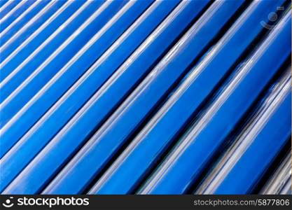 A diagonal and up close view of the convection tubes of a solar geyser as they fill the horizontal frame to create an abstract background image of blue and black diagonal lines.