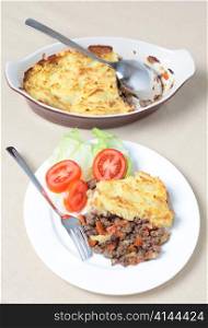 A dinner of shepherds pie or cottage pie and a salad with the serving dish seen from a high angle