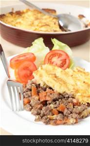 A dinner of shepherds pie or cottage pie and a salad with the serving dish in the background, vertical orientation