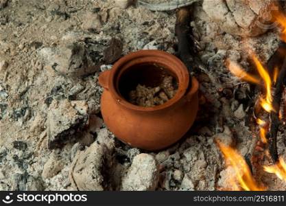 a dish in a clay pot is prepared on burning coals. the dish is cooked and smoked on charcoal. a dish on cold coals