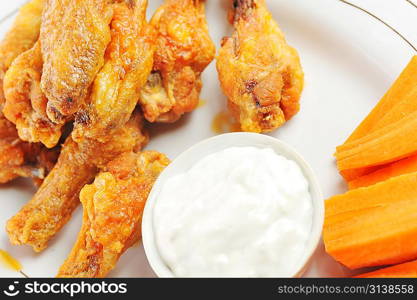 A dish of chicken hot wings and carrots with dipping sauce