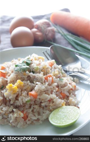 A dish of fried rice, carrot and egg on brown fabric, spoon, folk and ingredients for background