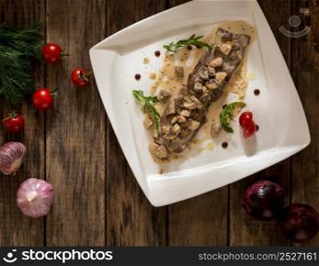 a dish of meat and mushrooms seasoned with gravy on a square plate, top view. dish on a wooden surface