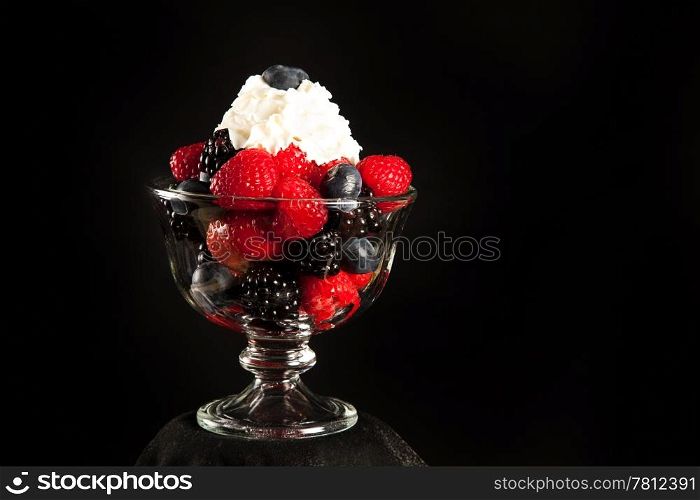 A dish of mixed berries and whipped cream over a black background, with room for text.
