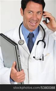 A doctor holding a laptop and having a conversation via his mobile phone.