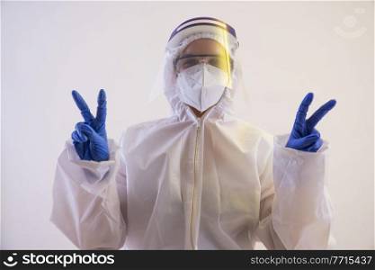 A doctor in PPE kit showing the gesture of victory with both hands.