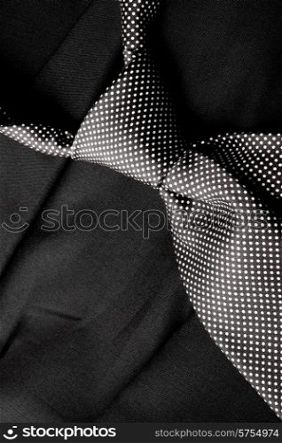 A dotted black and white tie that has been knotted lies loosly on a dark suite