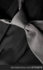A dotted black and white tie that has been knotted lies loosly on a dark suite