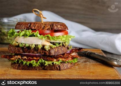 A double sandwich made of Greek bread with slices of fried bacon, avocado, boiled chicken breast, and tomatoes.. Double sandwich with chicken and bacon