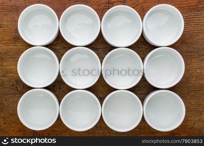 a dozen of empty white ceramic tasting bowls against rustic wood