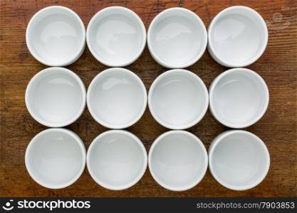 a dozen of empty white ceramic tasting bowls against rustic wood