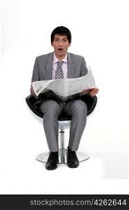 A dumbfounded businessman reading the newspaper.