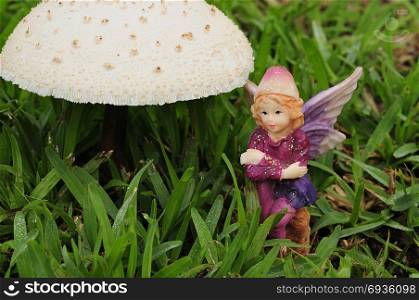 A fairy figurine sitting next to a mushroom in the garden