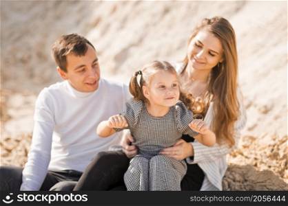 A family of three is sitting among mountains of sand.. A young family is sitting among the sandy mountains 3358.