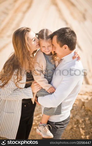 A family poses standing on a mountain of sand against the sky.. A young family with a daughter among the sand and blue sky 3307.