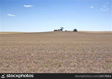 a farm house at the top of a dry field in the drought. dry farm