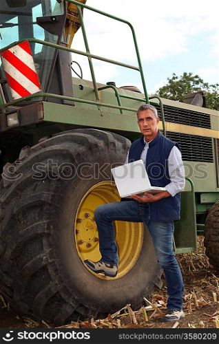 a farmer and his laptop near a combine harvester