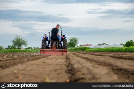 A farmer drives a tractor and cultivates an agricultural field. Milling soil, crushing before cutting rows. Farming, agriculture. Loosening surface, land cultivation. Plowing field.