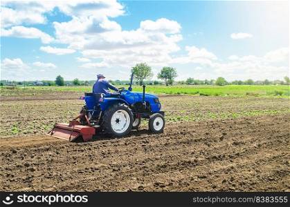A farmer on a tractor mills the soil with a milling machine equipment. Grinding loosening soil, removing plants and roots from last harvest. Growing vegetables. Ground crumbling and mixing.