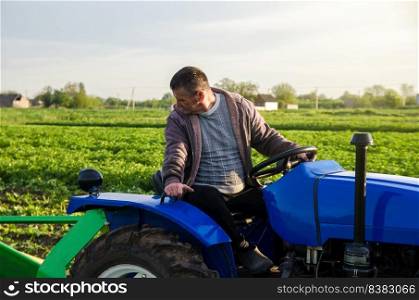 A farmer on a tractor monitors the operation of equipment for harvesting potatoes. Farming and farmland. Simplify speed up work with technology and machines. Agro industry and agribusiness