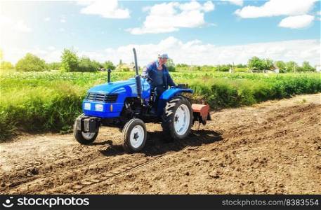 A farmer rides across the field on a tractor with a milling machine. Loosening surface, cultivating land for planting. Farming and agriculture. Work on the farm. Ground preparation for crop planting.
