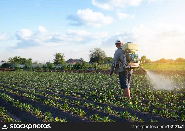 A farmer with a mist fogger sprayer sprays fungicide and pesticide on potato bushes. Effective crop protection, impact on environmental. Protection of cultivated plants from insects and fungal.. A farmer with a mist fogger sprayer sprays fungicide and pesticide on potato bushes. Protection of cultivated plants from insects and fungal. Effective crop protection, impact on environmental.