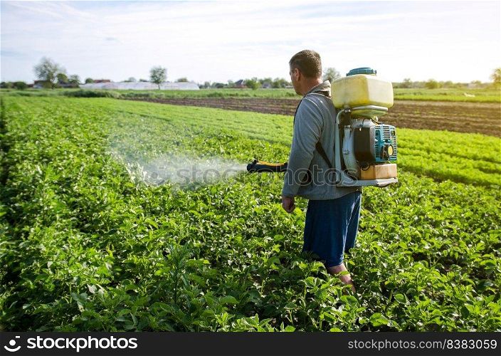 A farmer with a mist fogger sprayer sprays fungicide and pesticide on potato bushes. Protection of cultivated plants from insects and fungal infections. Effective crop protection, environmental impact