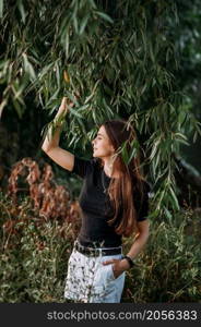 A fascinating girl among willow leaves on the shore of a pond.. A stylish beauty in a black T-shirt on the shore of a pond 3652.