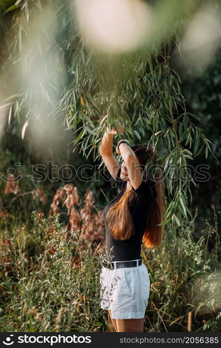 A fascinating girl among willow leaves on the shore of a pond.. A stylish beauty in a black T-shirt on the shore of a pond 3654.