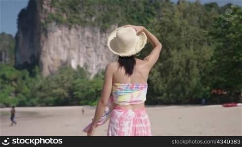 A fashionable pretty model strolling by a clean beach, showing a beautiful view of mountains and blue ocean, asia natural resources, spending time on vacation, healthy leisure activity on holiday