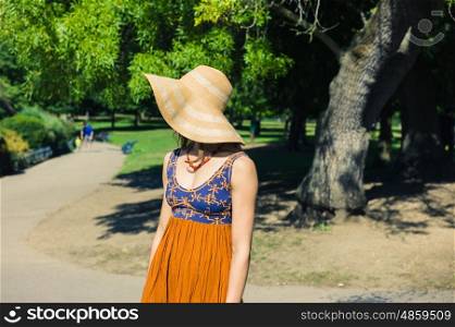 A fashionable young woman wearing a hat is standing in the park on a sunny summer day