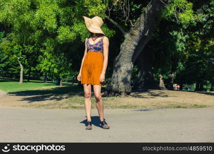 A fashionable young woman wearing a hat is standing in the park on a sunny summer day