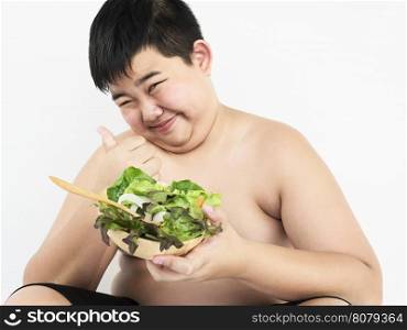A fat boy is happily eating vegetable salad