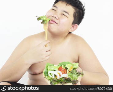 A fat boy is happily eating vegetable salad