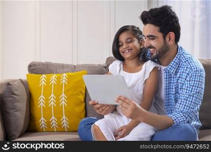 A FATHER AND DAUGHTER LAUGHING TOGETHER WHILE USING DIGITAL TABLET