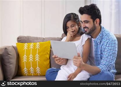 A FATHER AND DAUGHTER SITTING TOGETHER AND ENJOYING USING DIGITAL TABLET