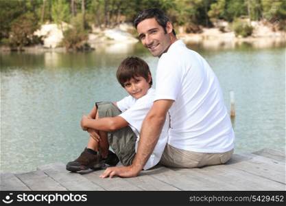 a father and his son seated on a pontoon faces a lake