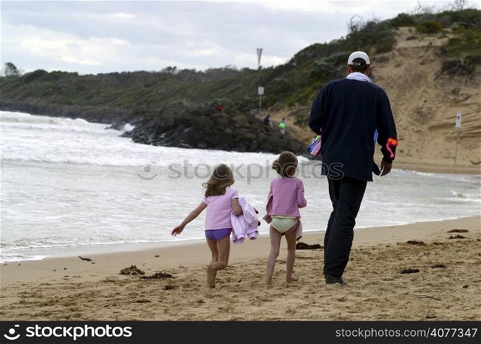 A father and his two young children walk along the beach. Father, children, family, holiday, walking, leasure, lifestyle, beach, coast, coastal,