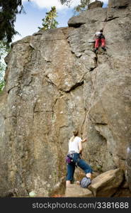 A female belaying a male on a steep rock face.