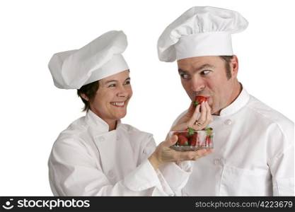 A female chef feeding strawberries to a male chef. Isolated on white. Focus on the female chef.