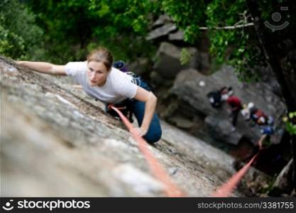 A female climber on a steep rock face. Shallow depth of field is used to isolated the climber. Focus is on the head, shoulders and arms of the climber.
