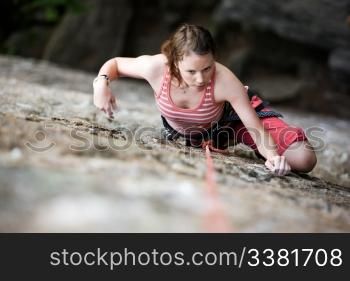 A female climber on a steep rock face viewed from above with the belayer in the background. Shallow depth of field is used to isolated the climber.