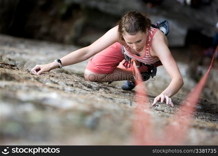 A female climber on a steep rock face viewed from above with the belayer in the background. Shallow depth of field is used to isolated the climber.