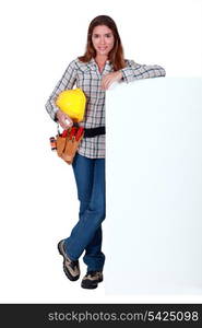 A female construction worker by a billboard.