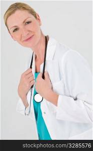 A female doctor dressed in scrubs and a white coat looking happily to camera