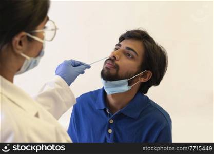 A female doctor performing the swab test for corona on a young man.