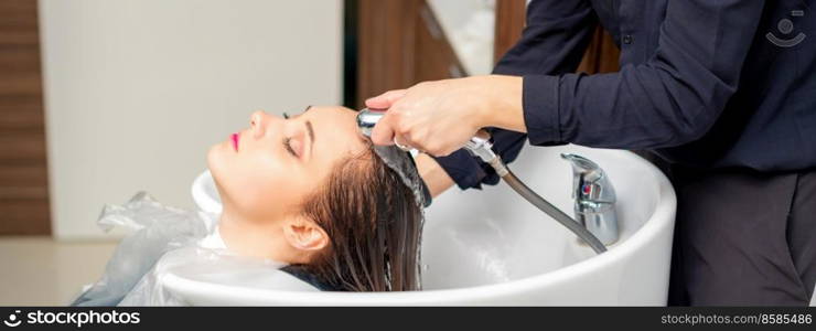 A female hairdresser is rinsing the hair of a young woman in a sink after sh&ooing in a hair salon. Hairdresser is rinsing the hair