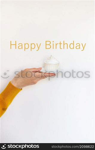 A female hand holds a delicious cupcake, congratulations on a happy birthday. Happy birthday lettering. A female hand holds a delicious cupcake, congratulations on a happy birthday. Happy birthday lettering.