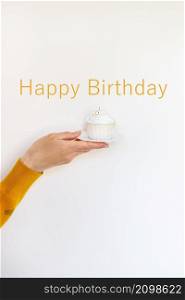 A female hand holds a delicious cupcake, congratulations on a happy birthday. Happy birthday lettering. A female hand holds a delicious cupcake, congratulations on a happy birthday. Happy birthday lettering.